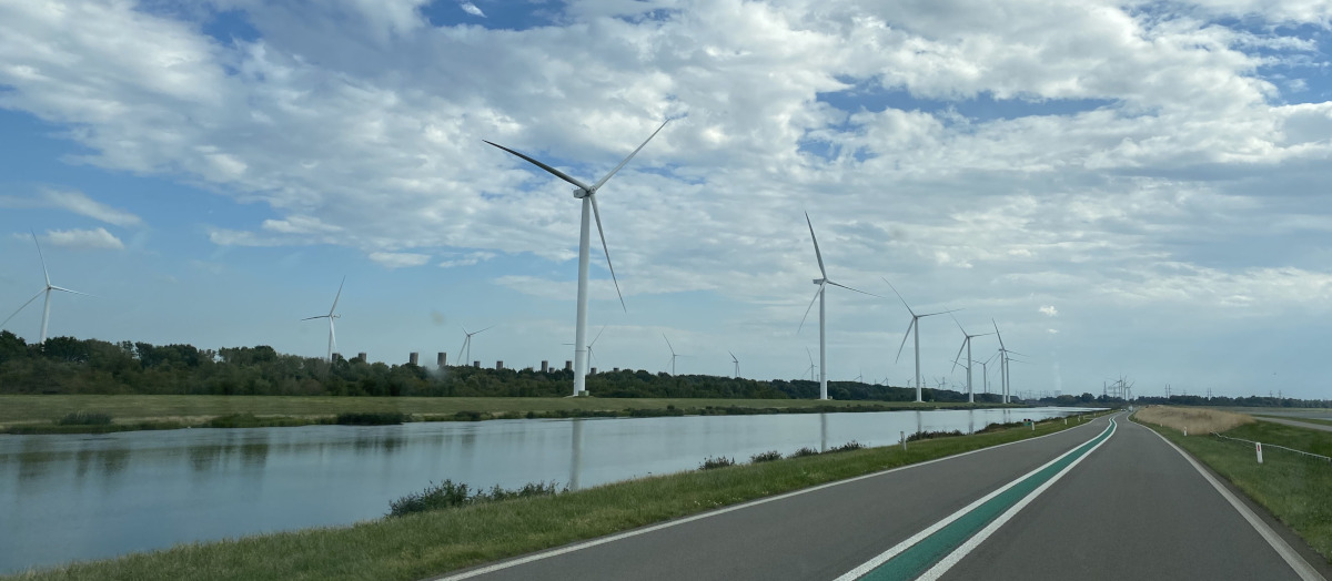 route bordée d'éoliennes à côté d'un fleuve et centrale nucléaire en activité en bout de route